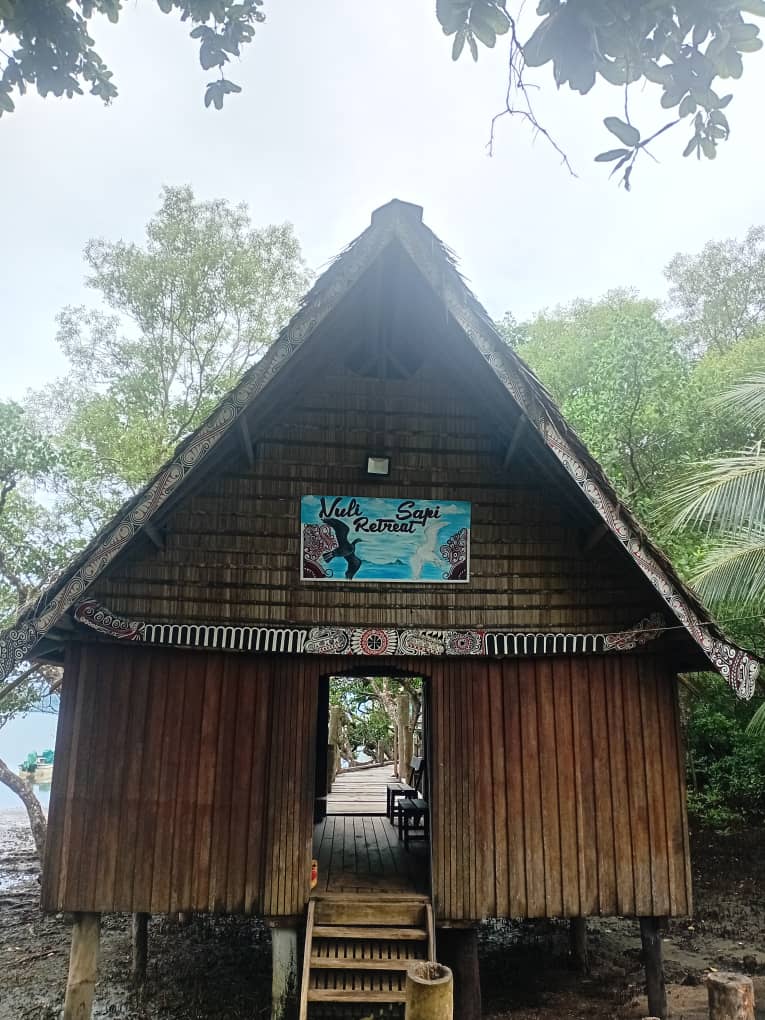 Front facade of a timber stilt building with central walkway entrance.
